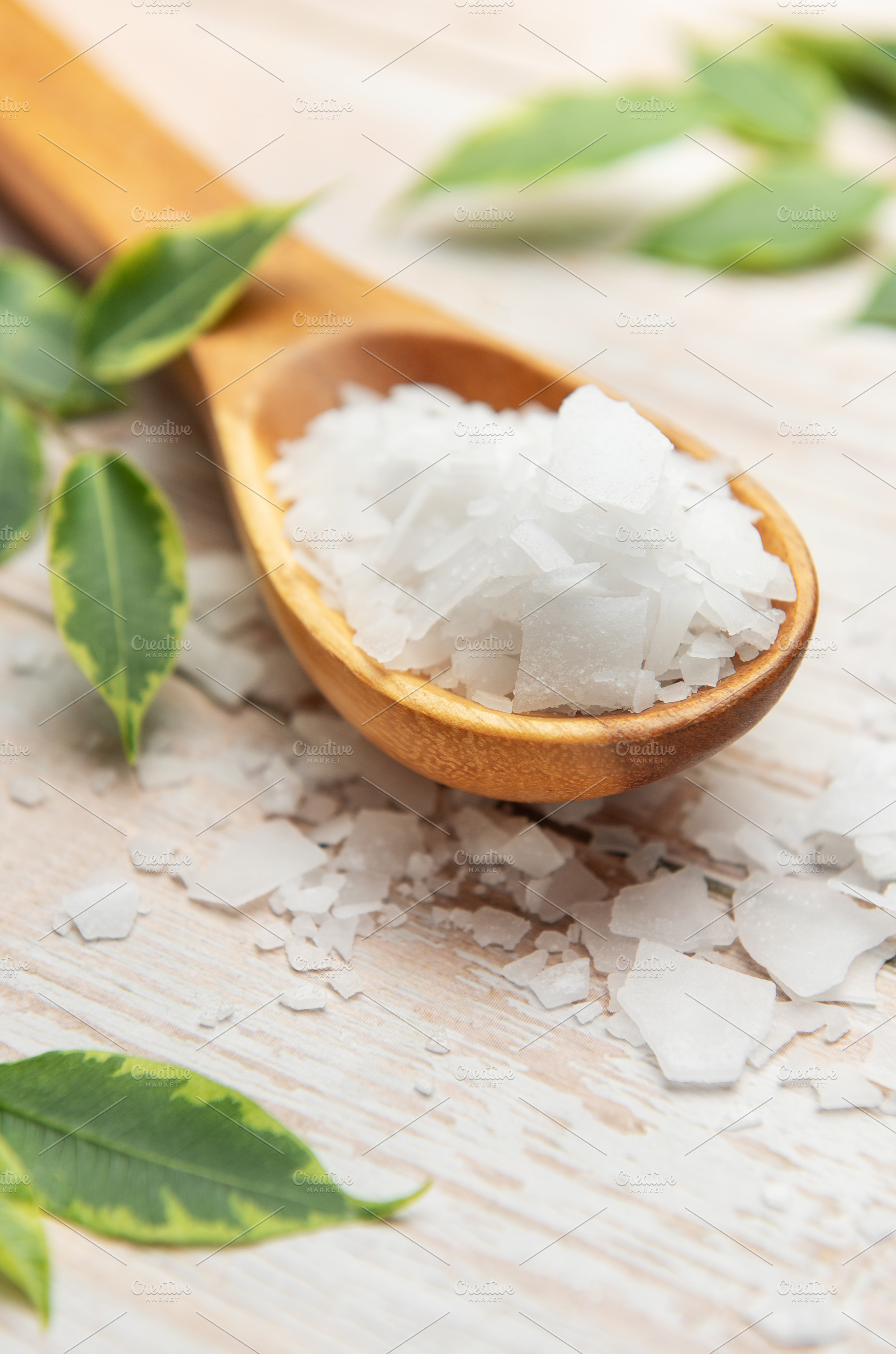 Magnesium chloride flakes on wooden spoon with green leaves, a Health & Medical Photo by Olena Rudo