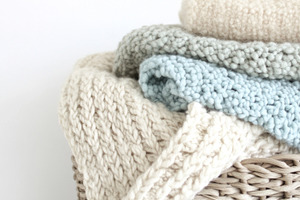 Pastel-colored knitted blankets stacked in basket on white backg, a Photo by Dvoevnore photos