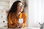 Smiling Arabic Lady Using Smartphone Looking Aside Sitting At Workplace, a Photo by Prostock-Studio (Thumbnail 4 of 4)