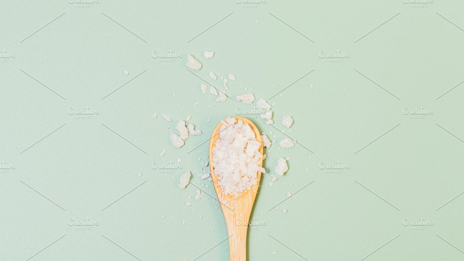 Sea salt crystals in wooden spoon on green background, a Beauty & Fashion Photo by progressman