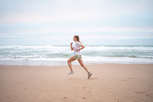 Determined sporty woman running on seashore at beach against sky, a Photo by andreonegin market