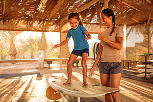 Girl balancing on a surfboard in a wooden beach shelter, a Person Photo by DanFLCreativo