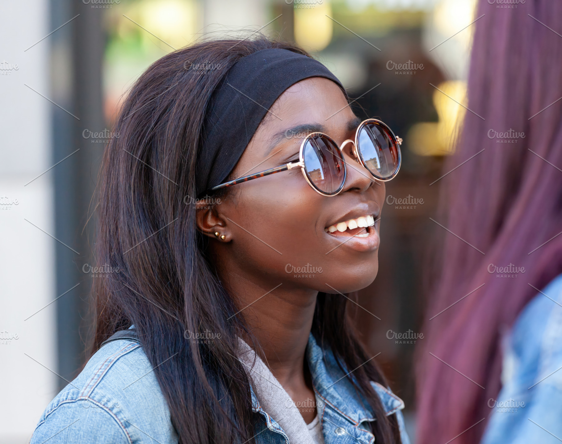 Young black woman wearing sunglasses smiling and chatting with a friend, an Abstract Photo by Antonio Gravante Market