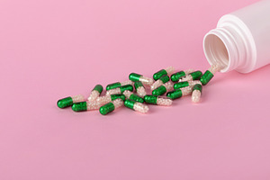 Green and white capsules spilling from a white bottle onto a pas, a Health & Medical Photo by Ales Munt