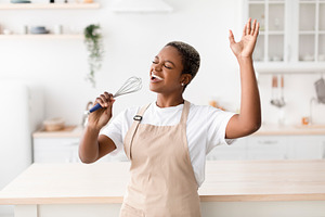 Happy inspired young african american woman in apron prepares food, sings at im, a Person Photo by Prostock-Studio