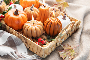 Autumn pumpkin candles burning in wicker tray on blanket