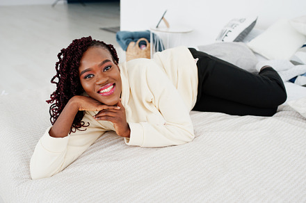 African woman in hoodie lying on the bed at home., a Person Photo by AS photostudio