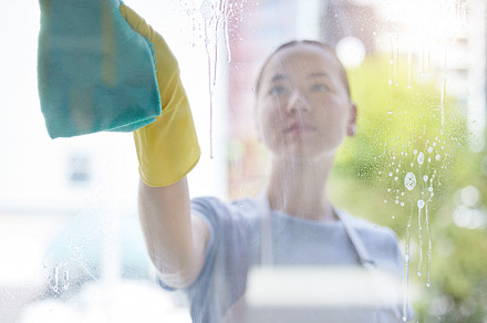 A beautiful young mixed race domestic worker using a cloth on a window. One Asian woman enjoying doing chores in her apartment, a Photo by Peopleimages.com