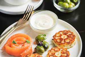 Savory Syrniki with Smoked Salmon, Olives and Sour Cream on White Plate