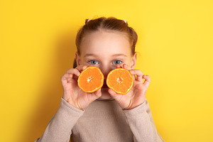 Smiling child holding two orange halves in front of eyes against, a Person Photo by Ales Munt