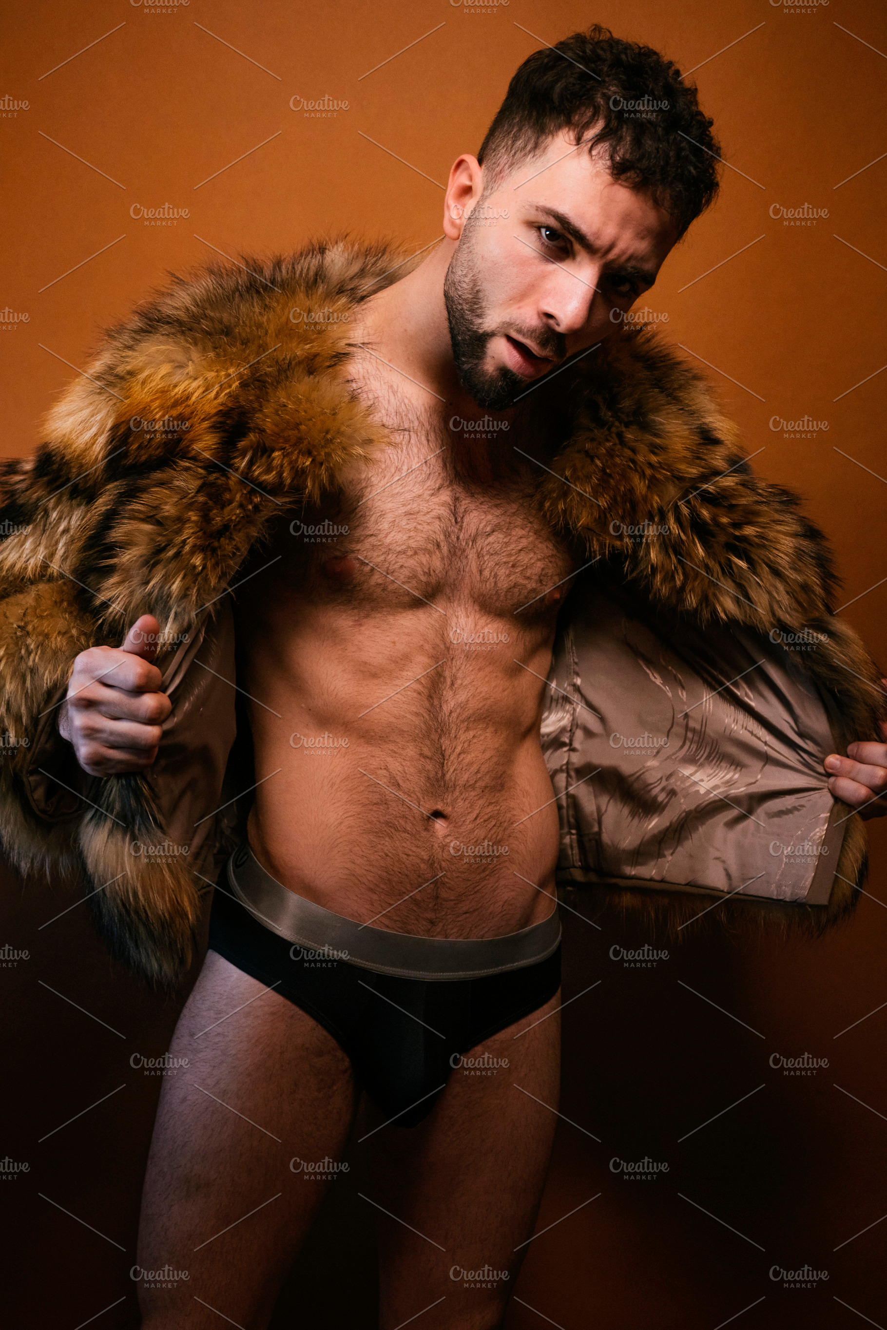 Muscular man wearing fur coat posing in studio, a Photo by karrastock