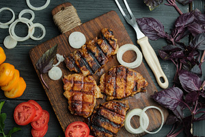 Grilled pork steaks on a wooden board, surrounded by vegetables, a Food & Drink Photo by ndanko