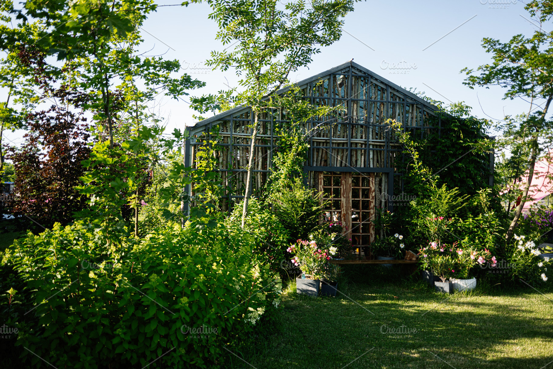 Cozy wooden greenhouse surrounded by lush green plants and colorful flowers, a Photo by AS photostudio