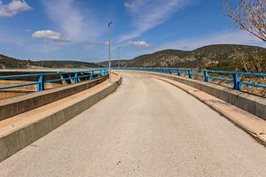Road over a dam with blue railings a, an Architecture Photo by Perpis