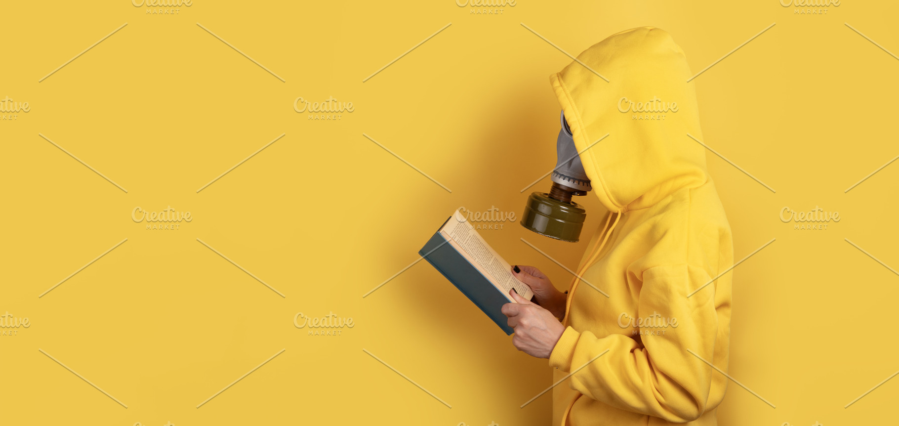 Side view of a person in yellow hoodie and gas mask reading a bo, a Person Photo by Ales Munt