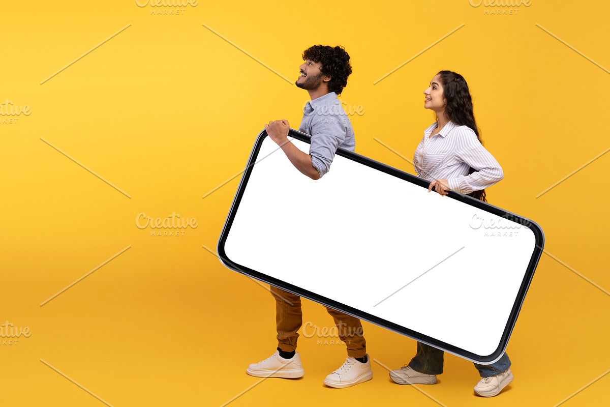 Young indian couple holding giant smartphone with mockup for design, yellow stu, a Photo by Prostock-Studio (Photo 3 of 4)