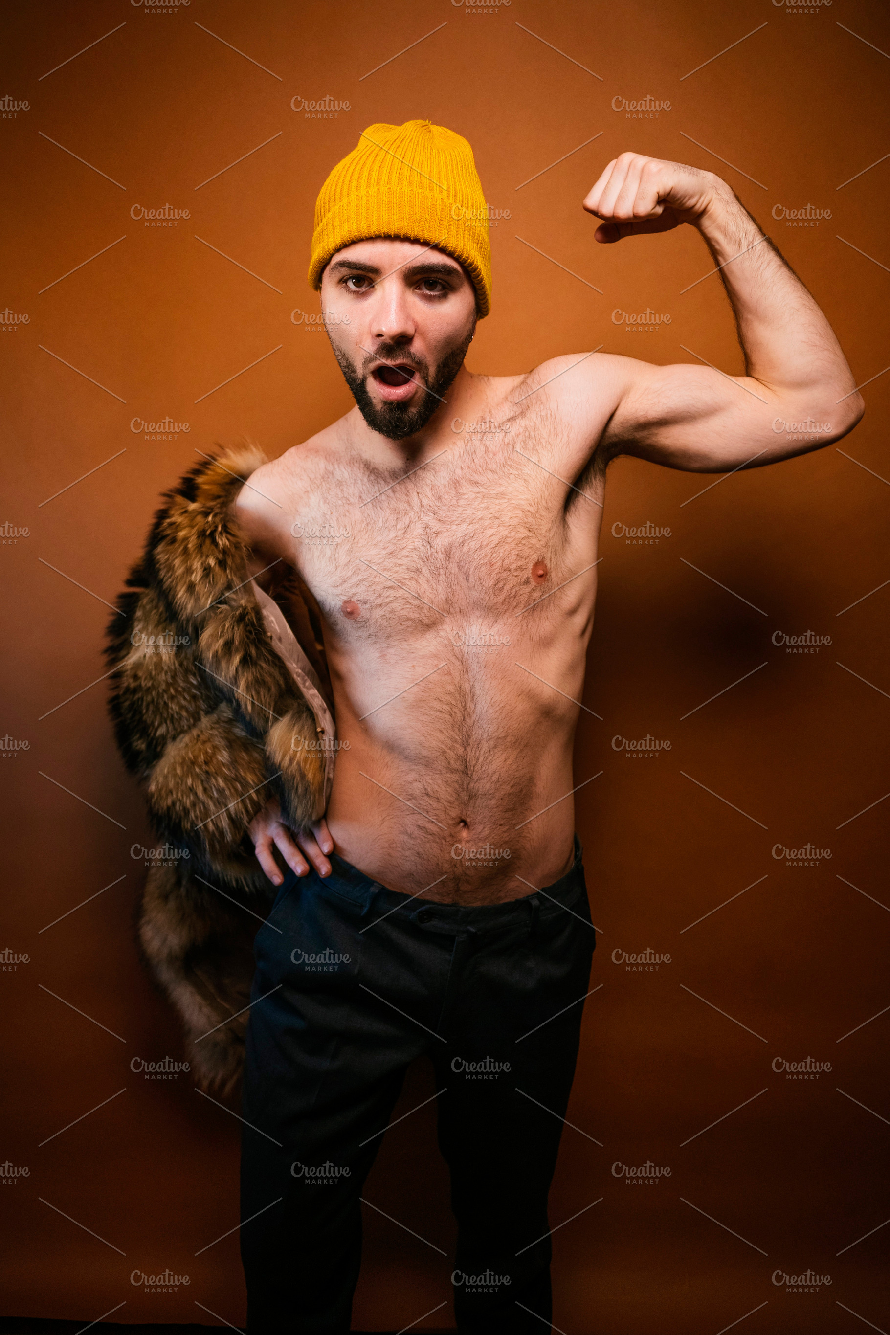 Confident man flexing muscle wearing yellow beanie, a Photo by karrastock