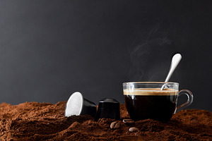 Glass cup of espresso on ground coffee and capsules front, a Food & Drink Photo by Davizro's Market