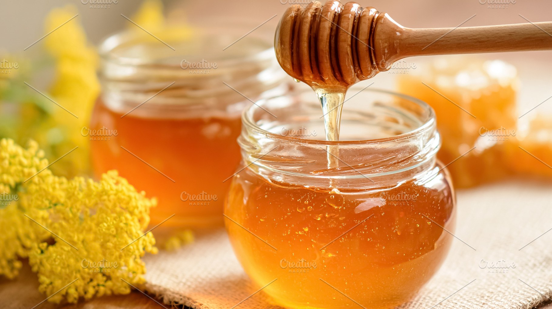 Golden honey dripping from dipper into small jar, surrounded by, a Photo by Studio ANNA