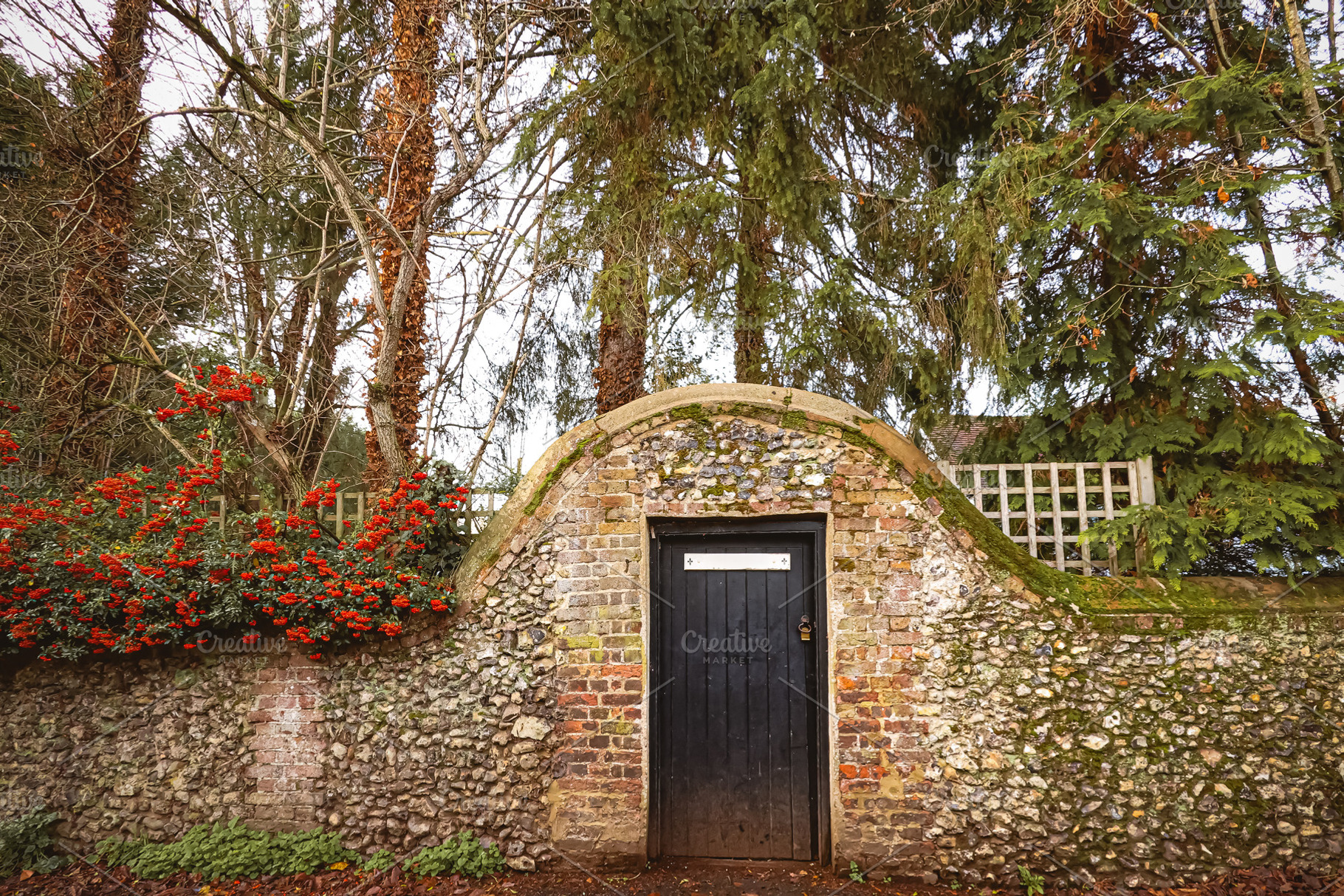Old weathered stone wall and brick archway enclosing a hidden black wooden door, a Photo by Studio ANNA