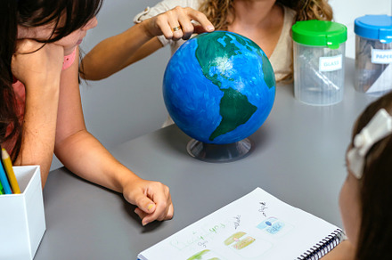 Female teacher giving ecology lesson with handmade globe world to girl students, a School & Education Photo by davidpereiras