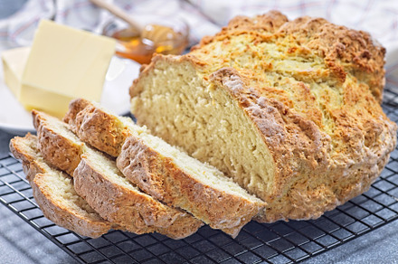 Freshly baked soda bread on cooling rack, sliced, butter and honey in the backg