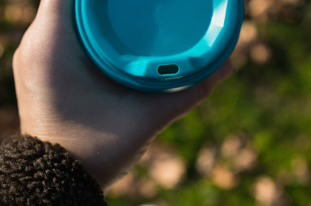 a glass with takeaway coffee in hands, against the background of blurry autumn