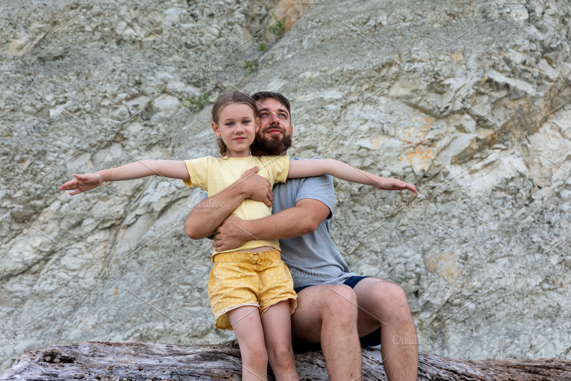 Father embraces his smiling daughter on a rocky backdrop, both looking joyful a, a Person Photo by Ales Munt