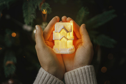 Little glowing house in hands on background of christmas tree li, a Holiday Photo by Sonjachni