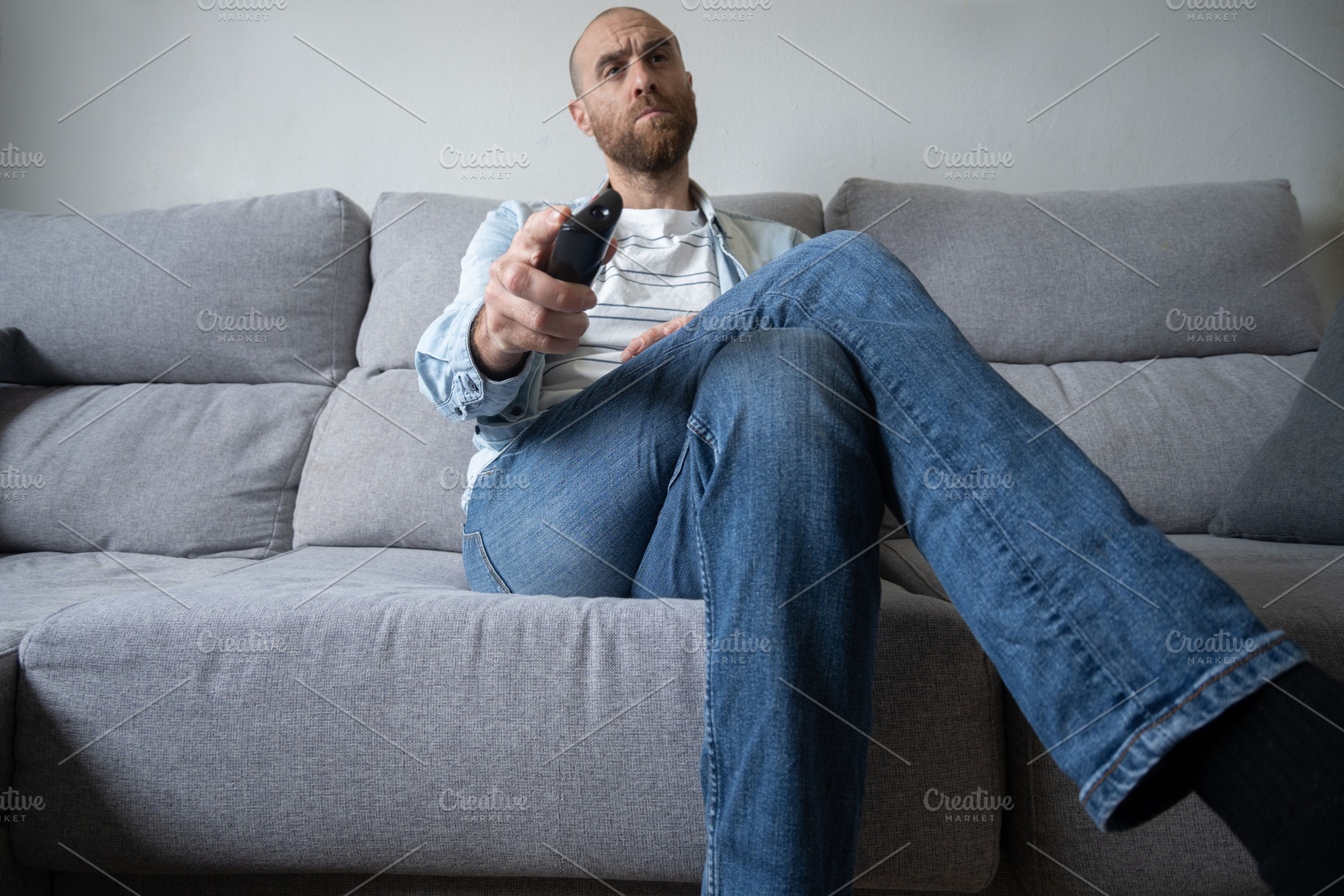 Man sitting on sofa watching TV with remote control at home, a Person Photo by etorres69