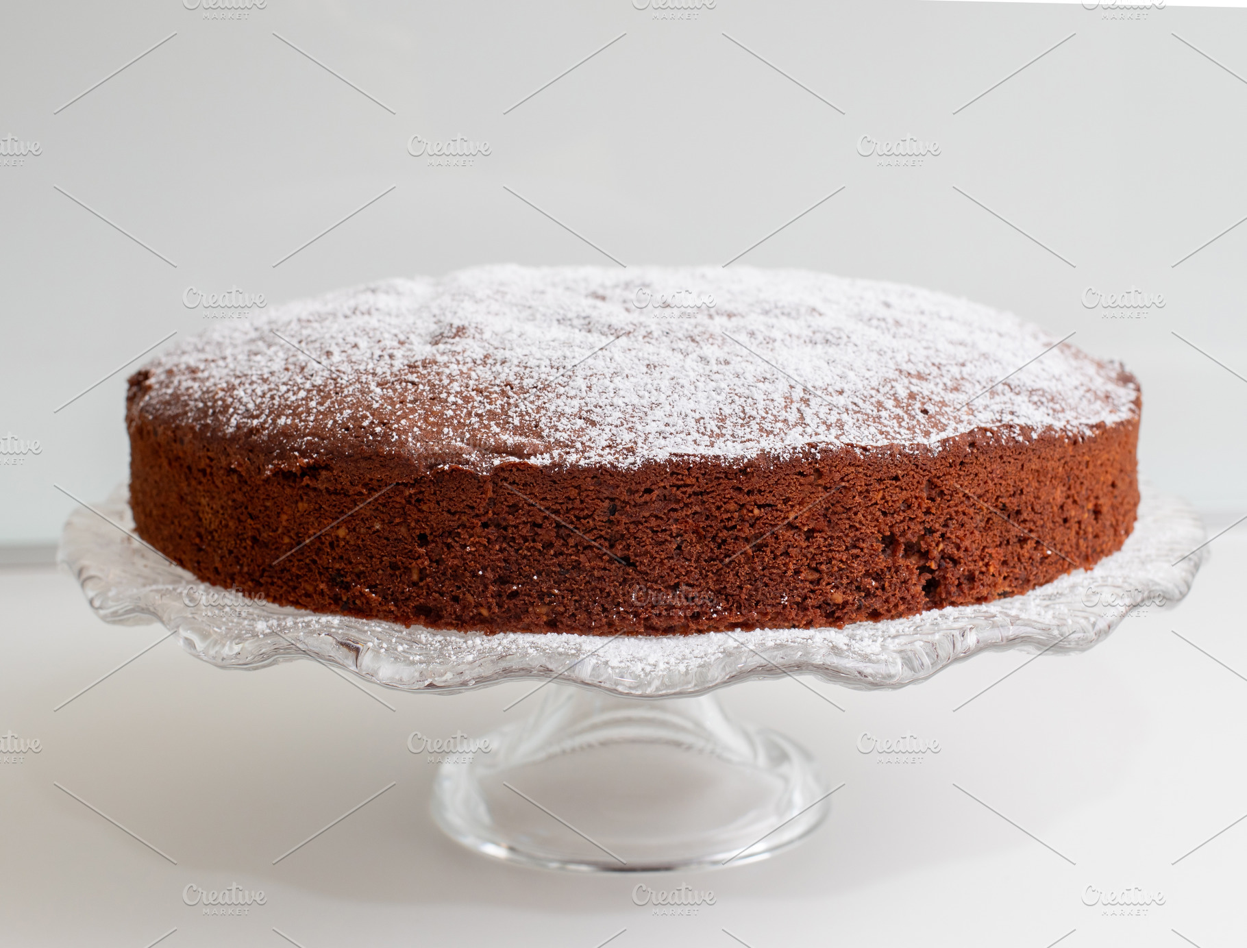 Delicious caprese cake resting on elegant glass cake stand, sprinkled with powd, a Food & Drink Photo by Antonio Gravante Market