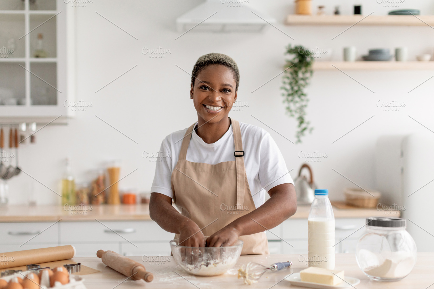 Cheerful young african american female chef blogger in apron making pie dough, a Photo by Prostock-Studio