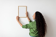 Lady Hanging Picture In Frame On Wall Decorating House Indoors, a Photo by Prostock-Studio (Thumbnail 3 of 4)