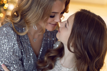 Mother and daughter in beautiful light dresses are standing at the Christmas tr, a Holiday Photo by SaulichPhoto
