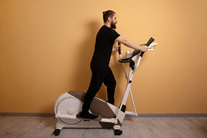 Bearded man in black sportswear using an elliptical trainer agai, a Person Photo by Ales Munt