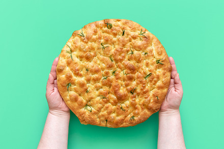 Focaccia with rosemary in woman hands, above view, a Food & Drink Photo by YesPhotographers