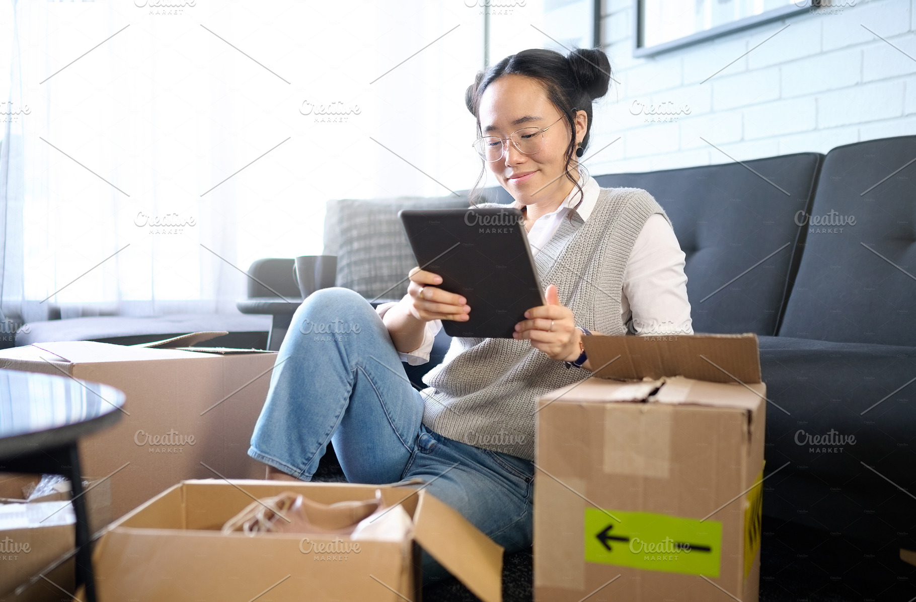 Tablet, real estate and Asian woman moving into new home while planning or calculating mortgage online. Relocation boxes, technology and female property owner or remote worker in living room of house, a Photo by Peopleimages.com