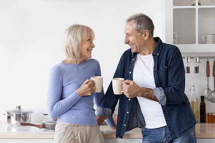Loving senior couple in homewear drinking coffee at kitchen, a Photo by Prostock-Studio