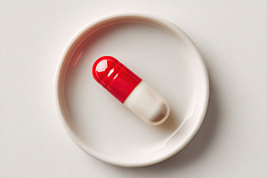 Close-up view of a single red and white capsule on a small dish against a plain, a Photo by AlyaAnd