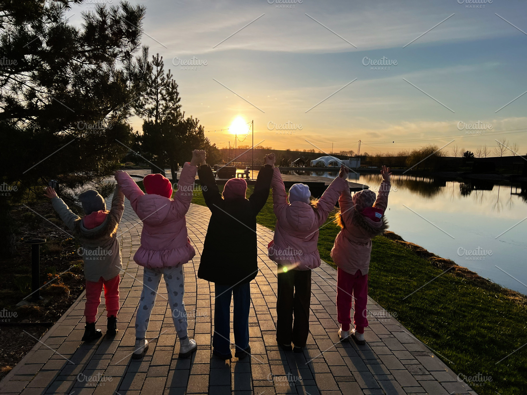 Children enjoying a sunset together by a peaceful riverside promenade, a Photo by AS photostudio