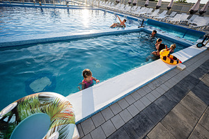 Family relaxing and swimming in a sunlit outdoor pool during summer, a Photo by AS photostudio