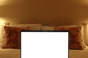 Laptop with a blank white screen resting on a bed in a cozy bedroom, featuring, a Photo by Studio ANNA