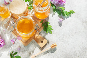 Golden acacia honey in jars with dipper, flowers, a Food & Drink Photo by Olena Rudo