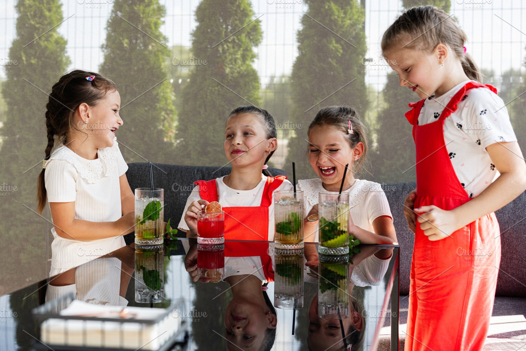 Four laughing children enjoying refreshing drinks together at a bright outdoors, a Photo by AS photostudio