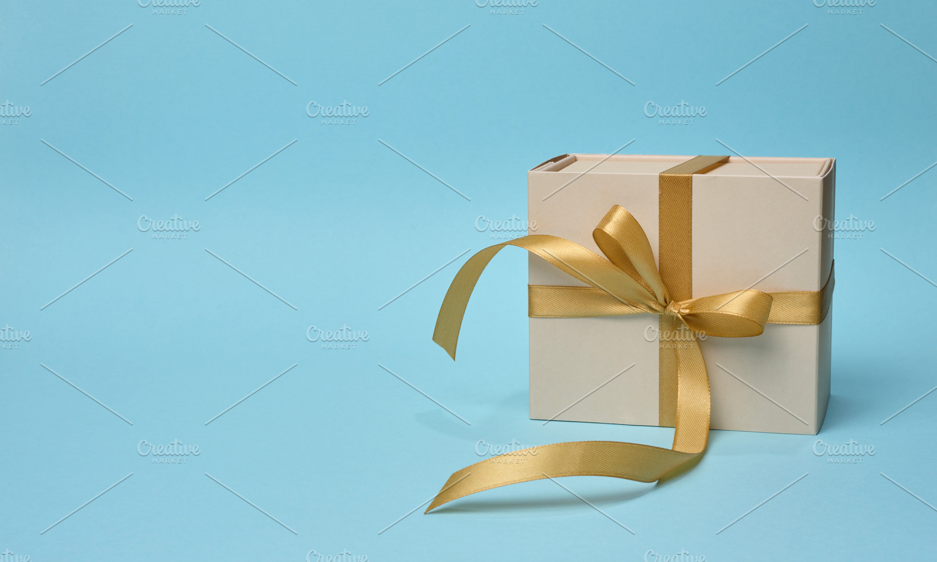 Gift box with a golden silk bow on a blue background, a Holiday Photo by ndanko