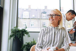 Smiling young businesswoman enjoying her coffee during an office