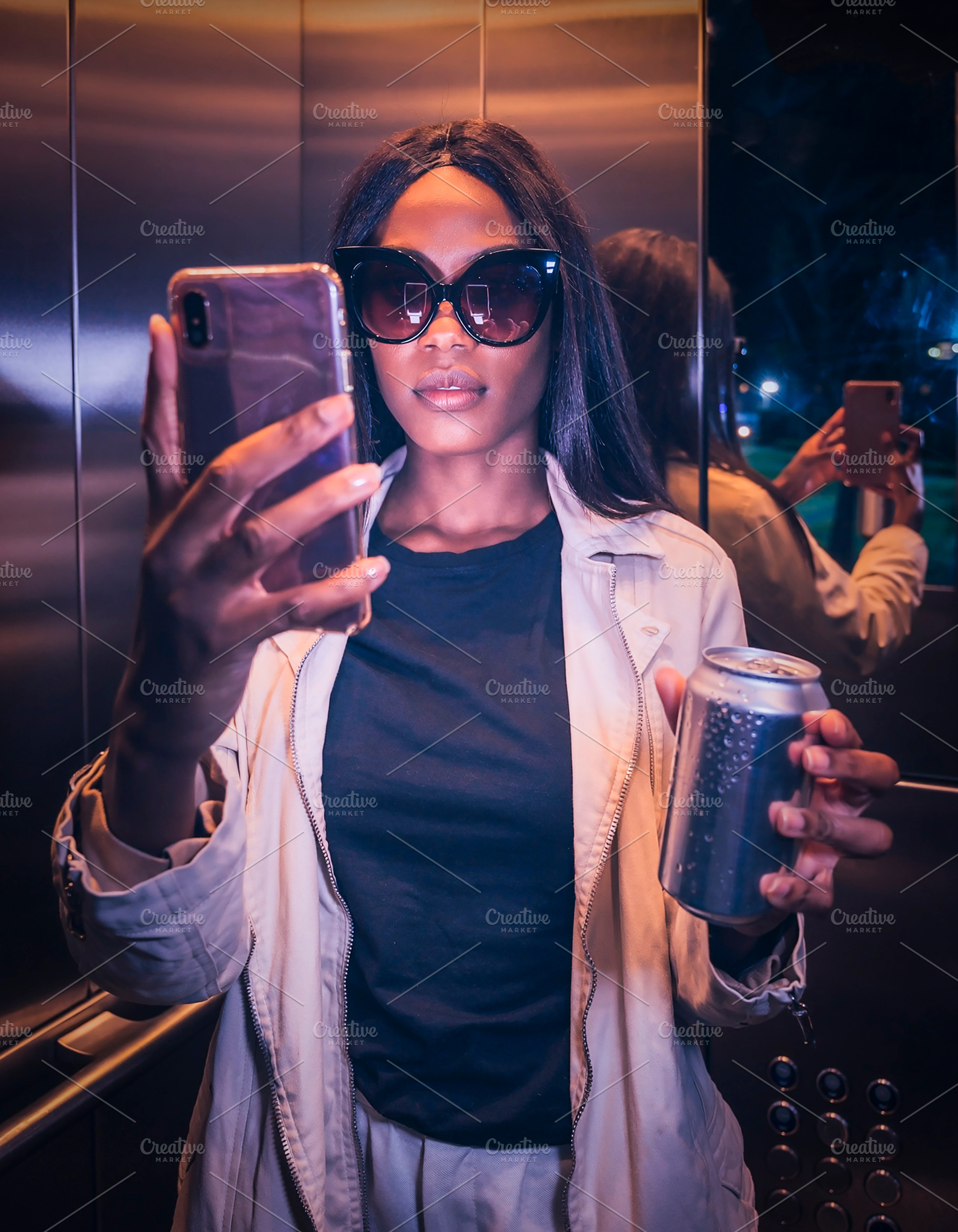 Woman on an elevator taking a selfie and holding a metallic soda, a Person Photo by DanFLCreativo