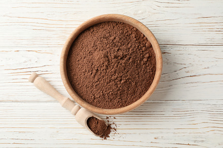 Wooden bowl and scoop with cocoa powder on white wood background, a Food & Drink Photo by AtlasStudio