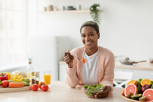 Cheerful millennial african american woman eating salad with organic vegetables, a Person Photo by Prostock-Studio