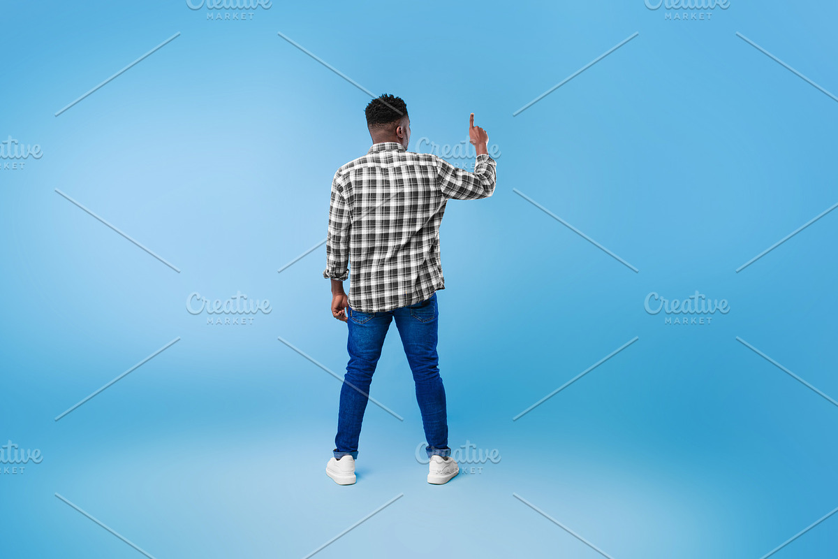 Back view of young black guy pushing button on virtual screen over blue studio, a Photo by Prostock-Studio (Photo 2 of 2)